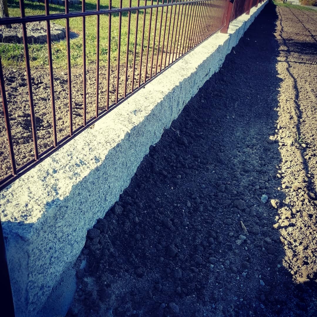 Granitowa obrzeże trawnika z metalowym ogrodzeniem, świeżo przygotowana ziemia pod nasadzenia, widok z bliska.