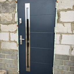 Welldoor Piotr Czerwonka - Montaż nowoczesnych, grafitowych drzwi zewnętrznych z przeszkleniem, widoczne uszczelnienie pianką montażową w surowym murze z betonu komórkowego.
