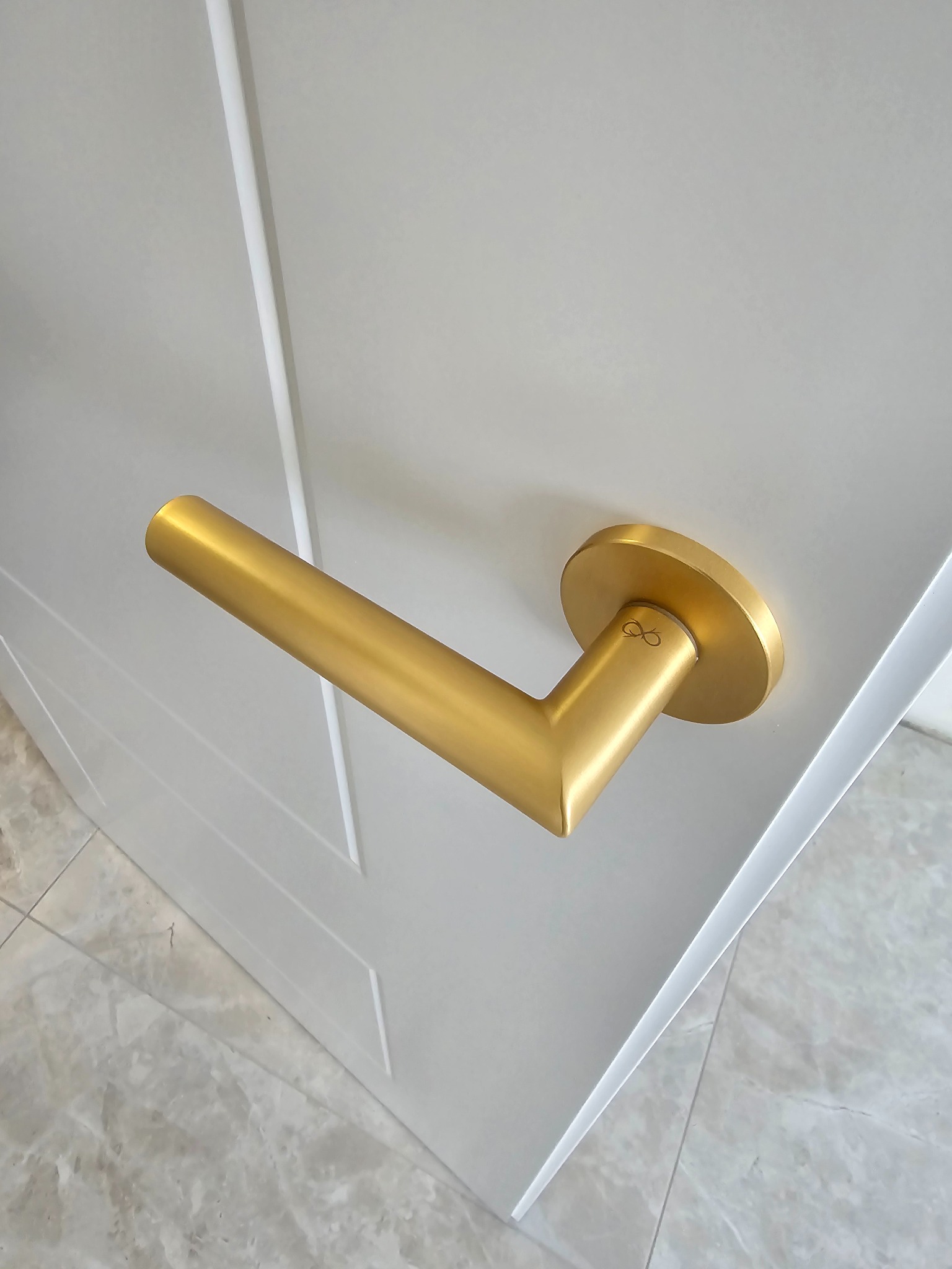 Detal złotej klamki na białych drzwiach wewnętrznych z dekoracyjnym frezowaniem i marmurową posadzką