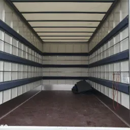 Wnętrze paki busa transportowego z zamontowanymi zabezpieczeniami ścian, widoczne mocowania i luźno leżące maty podłogowe.