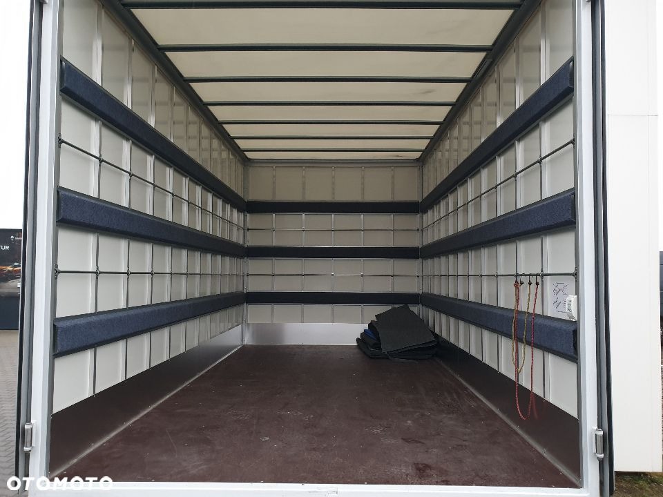 Wnętrze paki busa transportowego z zamontowanymi zabezpieczeniami ścian, widoczne mocowania i luźno leżące maty podłogowe.