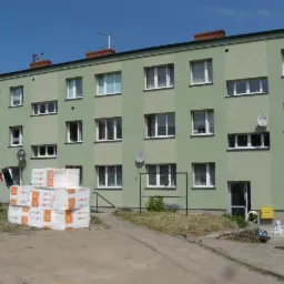 Trzypiętrowy budynek po renowacji elewacji, z ociepleniem widocznym w postaci spakowanych płyt styropianowych na placu budowy. Świeża, zielona elewacja.