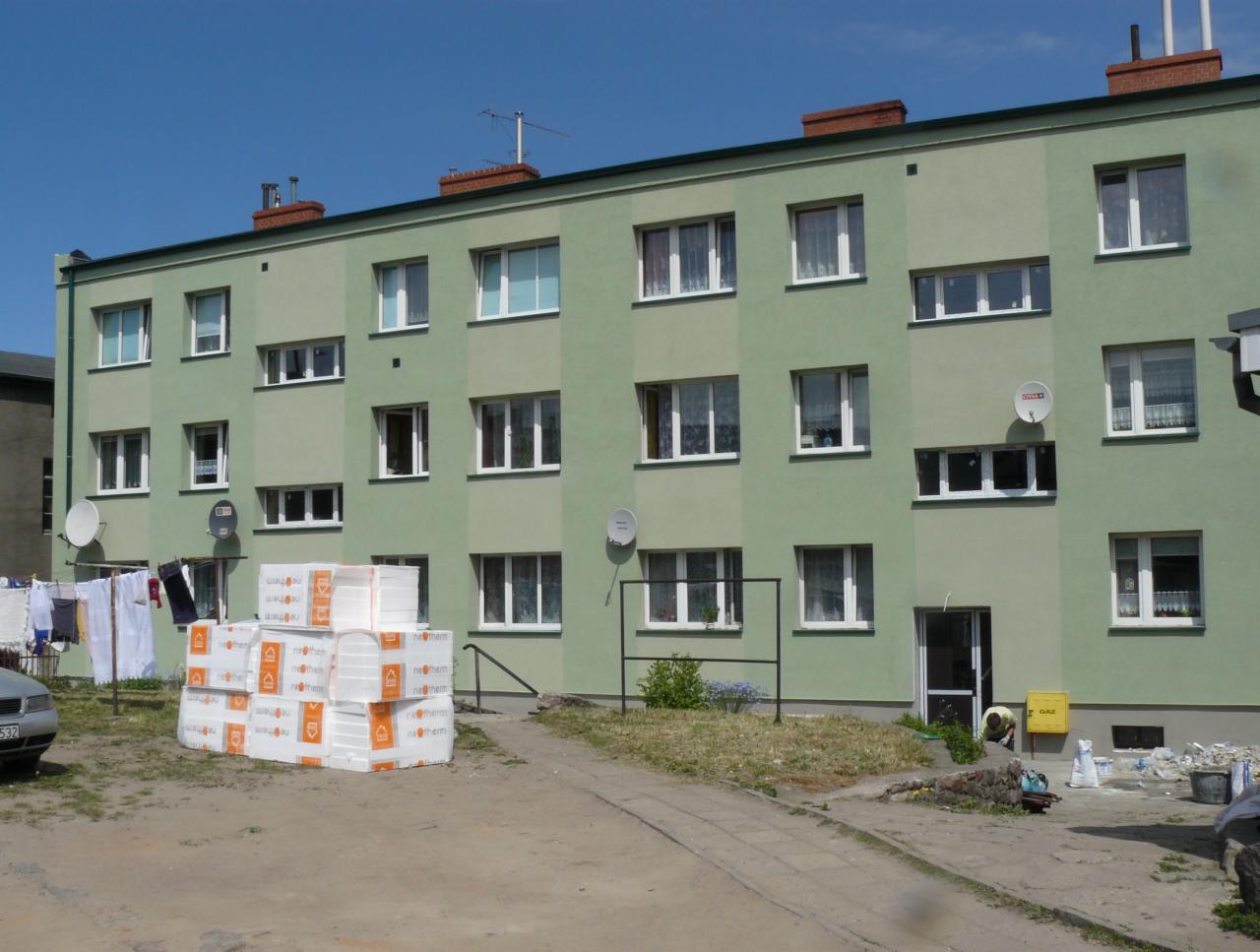 Trzypiętrowy budynek po renowacji elewacji, z ociepleniem widocznym w postaci spakowanych płyt styropianowych na placu budowy. Świeża, zielona elewacja.