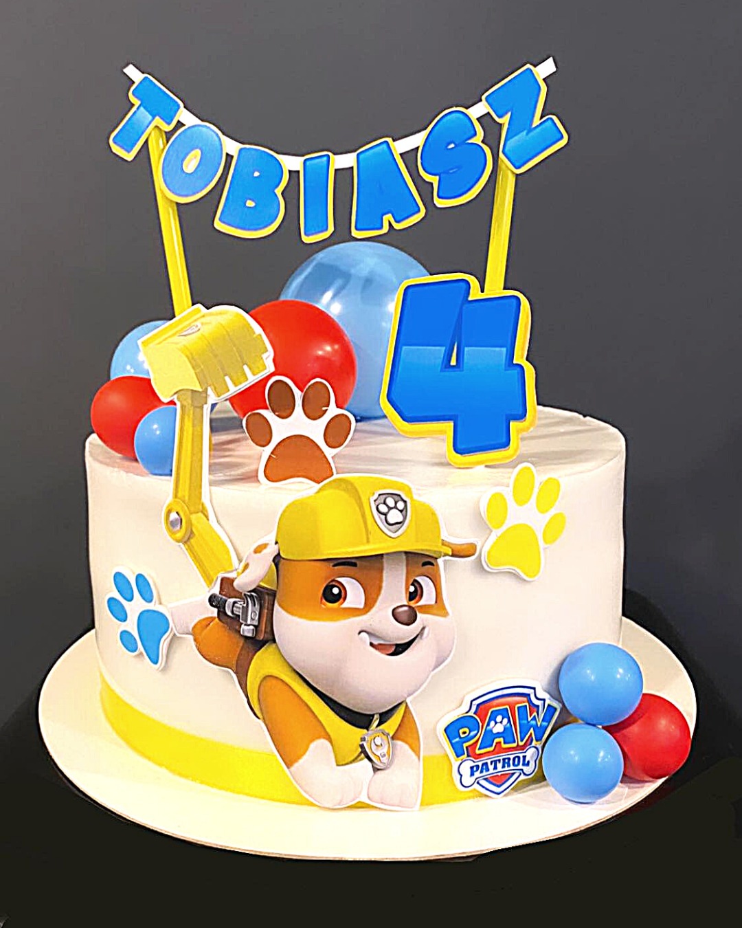 Tort urodzinowy z dekoracjami z bajki Psi Patrol, z imieniem Tobiasz i cyfrą 4, na białym tle.
