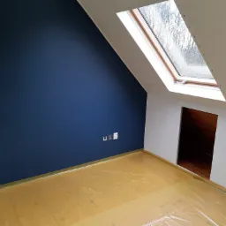 Poddasze z granatową ścianą, zabezpieczoną podłogą folią malarską, oknem dachowym i otwartym wejściem do schowka.