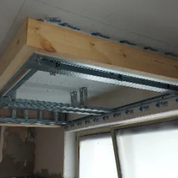 Konstrukcja sufitu podwieszanego z płyt karton gips, drewniana rama, metalowe profile, widoczne mocowania i okno w tle, w trakcie montażu.