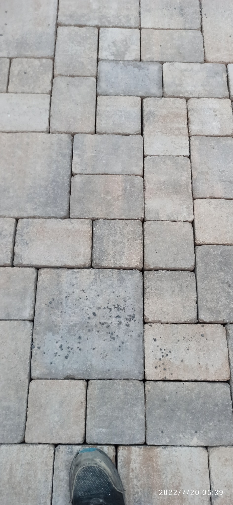 Ułożona szara kostka brukowa w regularny wzór, widoczny fragment buta roboczego w dolnej części kadru, data i godzina zdjęcia w prawym dolnym rogu.