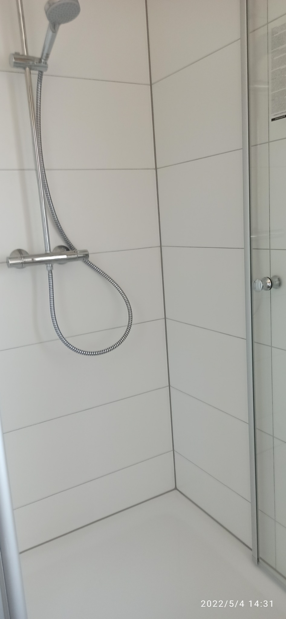 Kabina prysznicowa z chromowaną armaturą i deszczownicą, widok z góry na białe, poziome płytki.