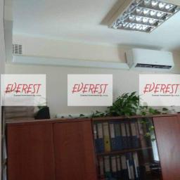 Everest Investment Sp. z o.o. - Klimatyzator ścienny zamontowany w biurze nad szafą z segregatorami, widoczna lampa sufitowa i kratka wentylacyjna, na zdjęciu nałożone logo firmy.