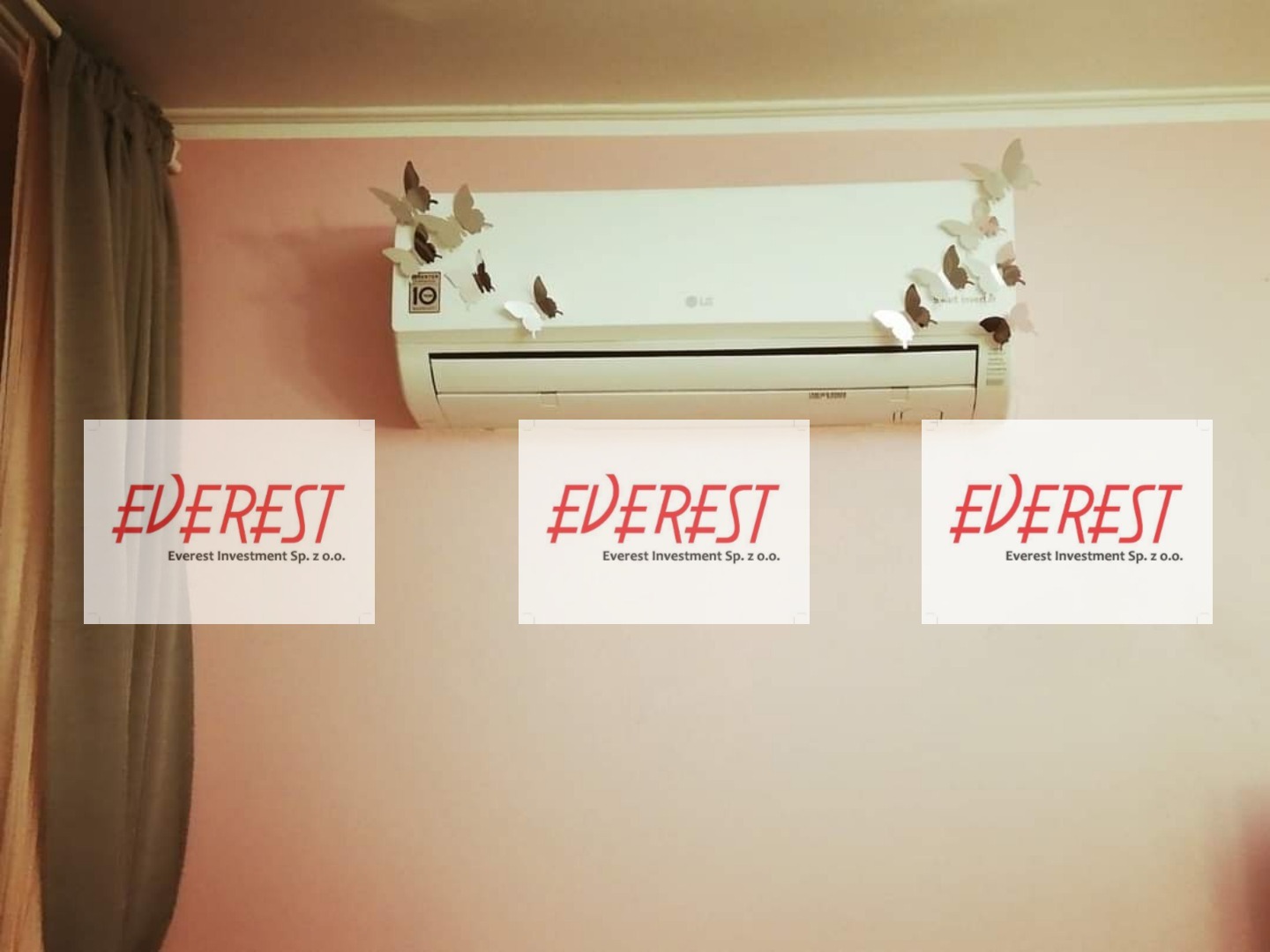 Biały klimatyzator LG na różowej ścianie, ozdobiony papierowymi motylami, zasłonięty trzema logotypami firmy Everest Investment Sp. z o.o.