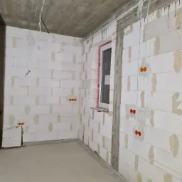 Surowy stan wnętrza w Bukowie z widocznymi przewodami elektrycznymi w ścianach z betonu komórkowego oraz przygotowanymi otworami pod gniazdka.