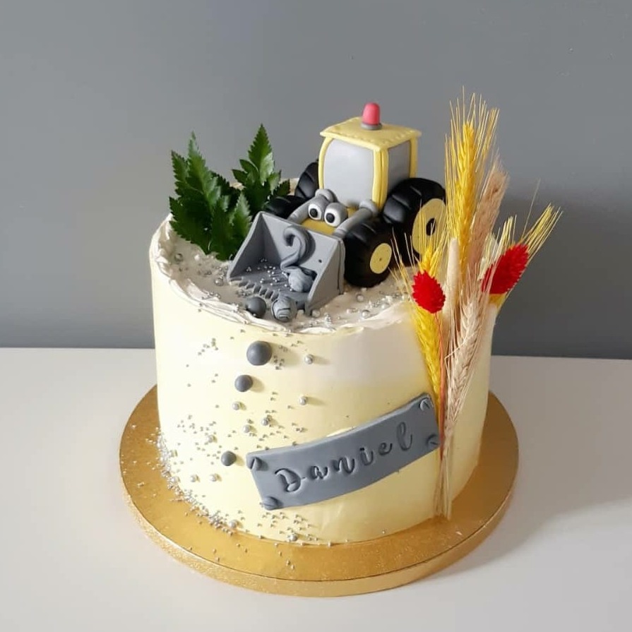 Tort urodzinowy z motywem traktora z masy cukrowej, dekorowany źdźbłami zbóż i imieniem Daniel, na złotym podkładzie.