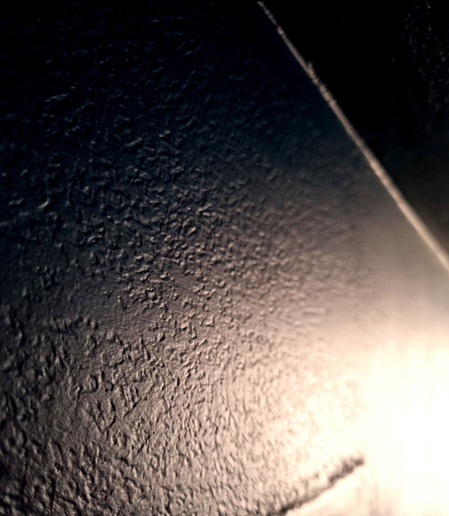 Zbliżenie na nierówną, ciemną powierzchnię wyłożoną płytkami z widoczną fugą i refleksem światła.