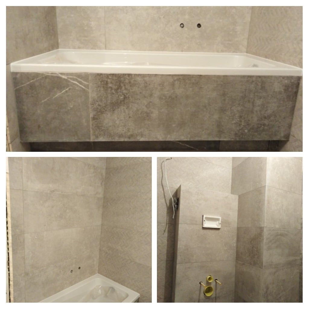 Obudowana płytkami wanna w łazience z szarymi płytkami, widoczne niedokończone prace elektryczne.