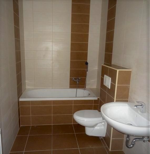 Ukończona łazienka w beżowo-brązowych odcieniach, z wanną, umywalką i toaletą, wyłożona płytkami ceramicznymi z pionowymi pasami dekoracyjnymi.