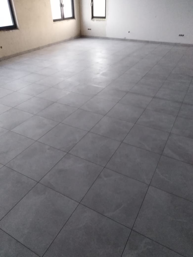 Wykończona podłoga z szarych, kwadratowych płytek w pustym pomieszczeniu z trzema oknami i białymi ścianami.