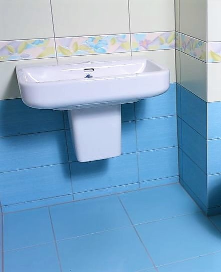 Biała umywalka ceramiczna zamontowana na niebieskich płytkach ściennych i podłogowych z dekoracyjnym pasem płytek z motywem kwiatowym w górnej części ściany.