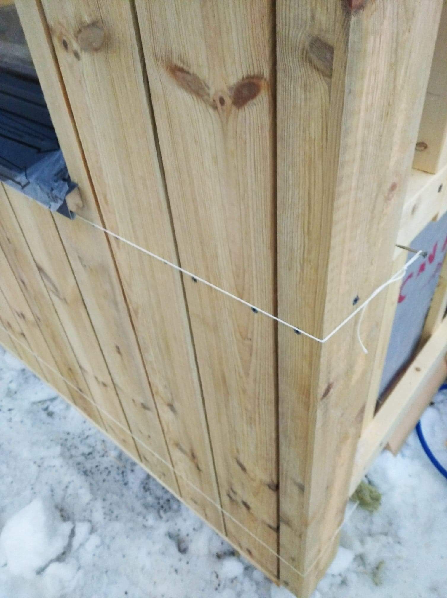 Konstrukcja drewniana z desek, narożnik budynku z widocznym sznurkiem poziomującym, tło ośnieżone.