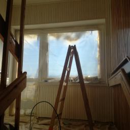 Pro-Jet - Przygotowanie do malowania wnętrza: okno zabezpieczone folią, drewniana drabina, podłoga przykryta płachtą malarską, widoczny fragment schodów i boazerii.