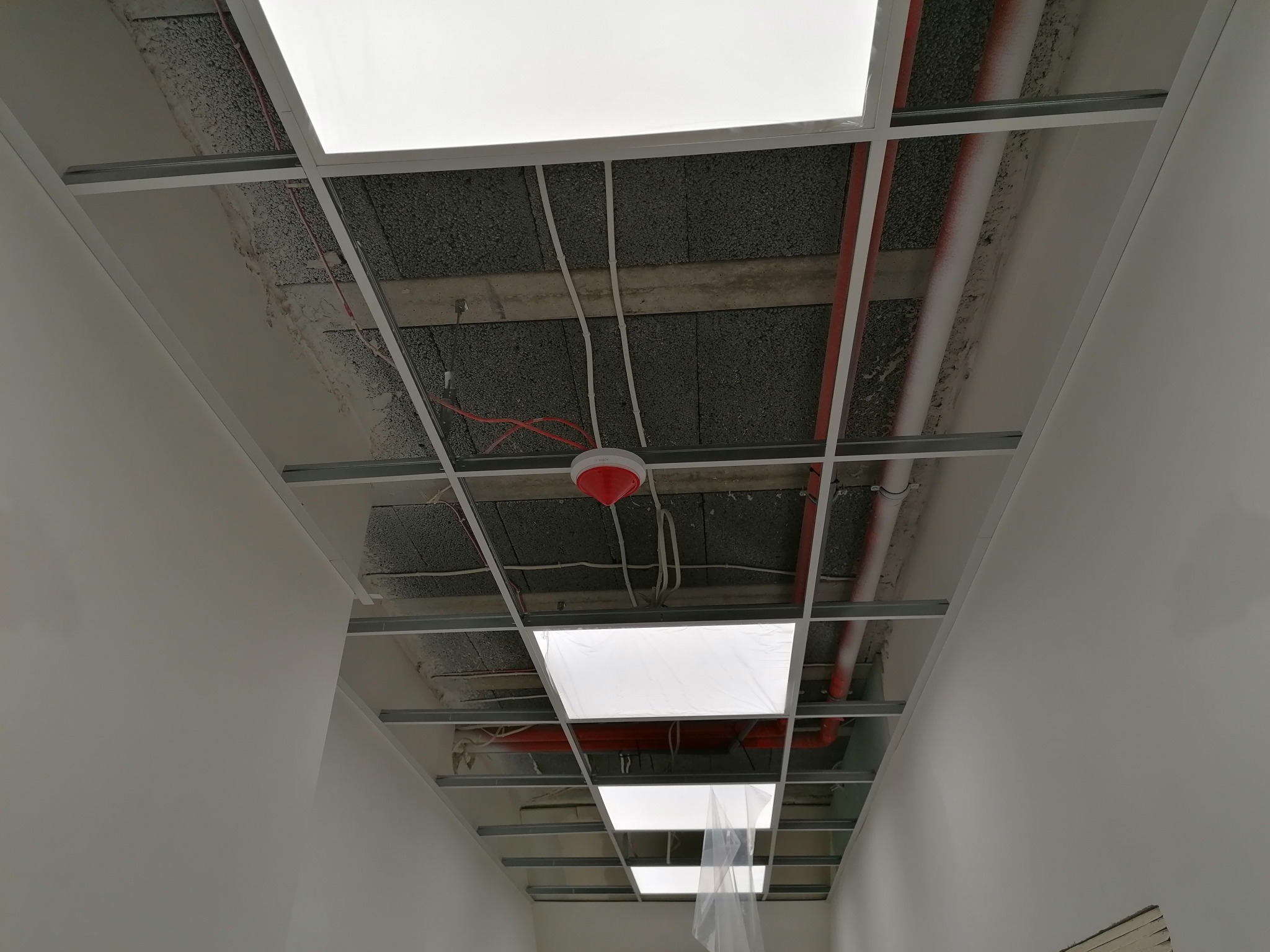 Montaż sufitu podwieszanego: widok na ruszt z profili metalowych, instalacje pod stropem i wbudowane panele oświetleniowe.