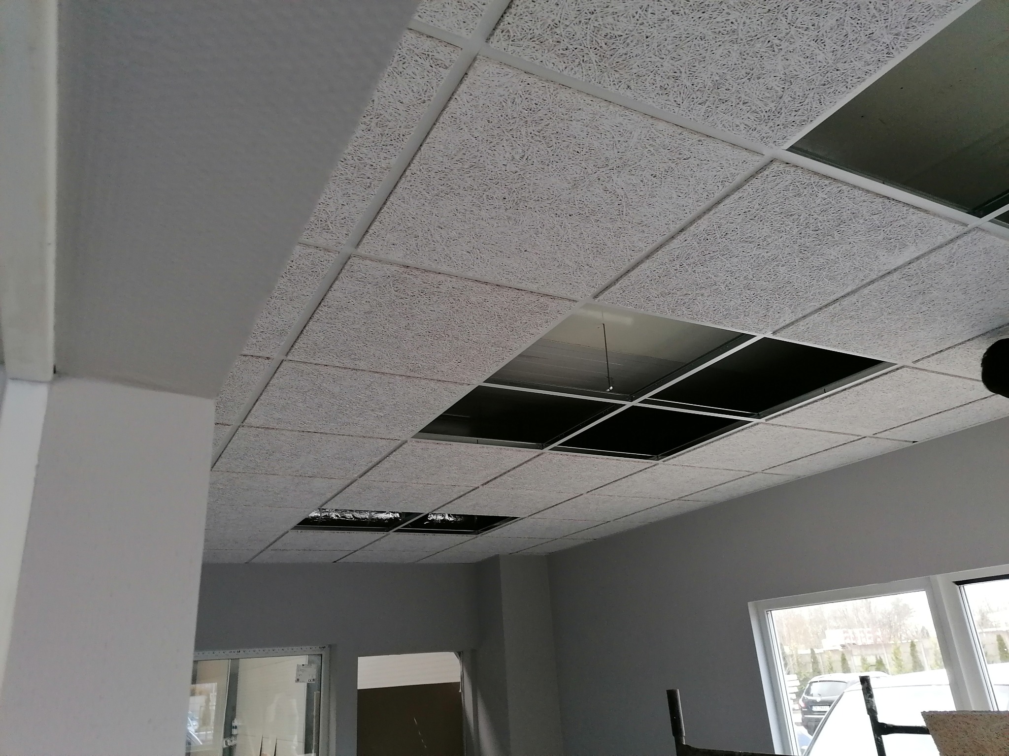 Montaż sufitu podwieszanego z płyt o strukturze włóknistej, widoczne odsłonięte elementy konstrukcji i fragment okna.