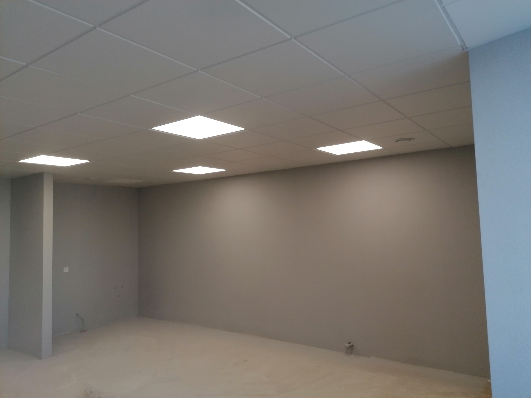 Wykończone wnętrze pokoju z szarą ścianą, sufitem z płyt kartonowo-gipsowych i wbudowanym oświetleniem LED.