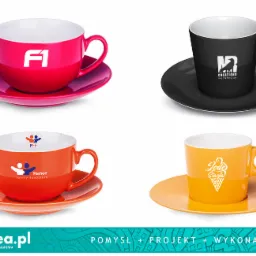 Zestaw czterech filiżanek z logotypami różnych firm, wykonanych w Zielonej Górze, każda filiżanka w innym kolorze z dopasowanym spodkiem, na białym tle.