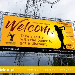 Billboard z napisem 'Welcome' i grafiką golfisty na tle zachodzącego słońca, promujący pole golfowe Kalinowe Pola z ofertą zrobienia selfie z banerem dla zniżki, widoczny na tle konstrukcji...