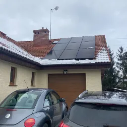 Instalacja paneli fotowoltaicznych Selfa 360W fullblack na dachu domu w Strzelinie, częściowo pokrytym śniegiem. Na pierwszym planie dwa zaparkowane samochody.