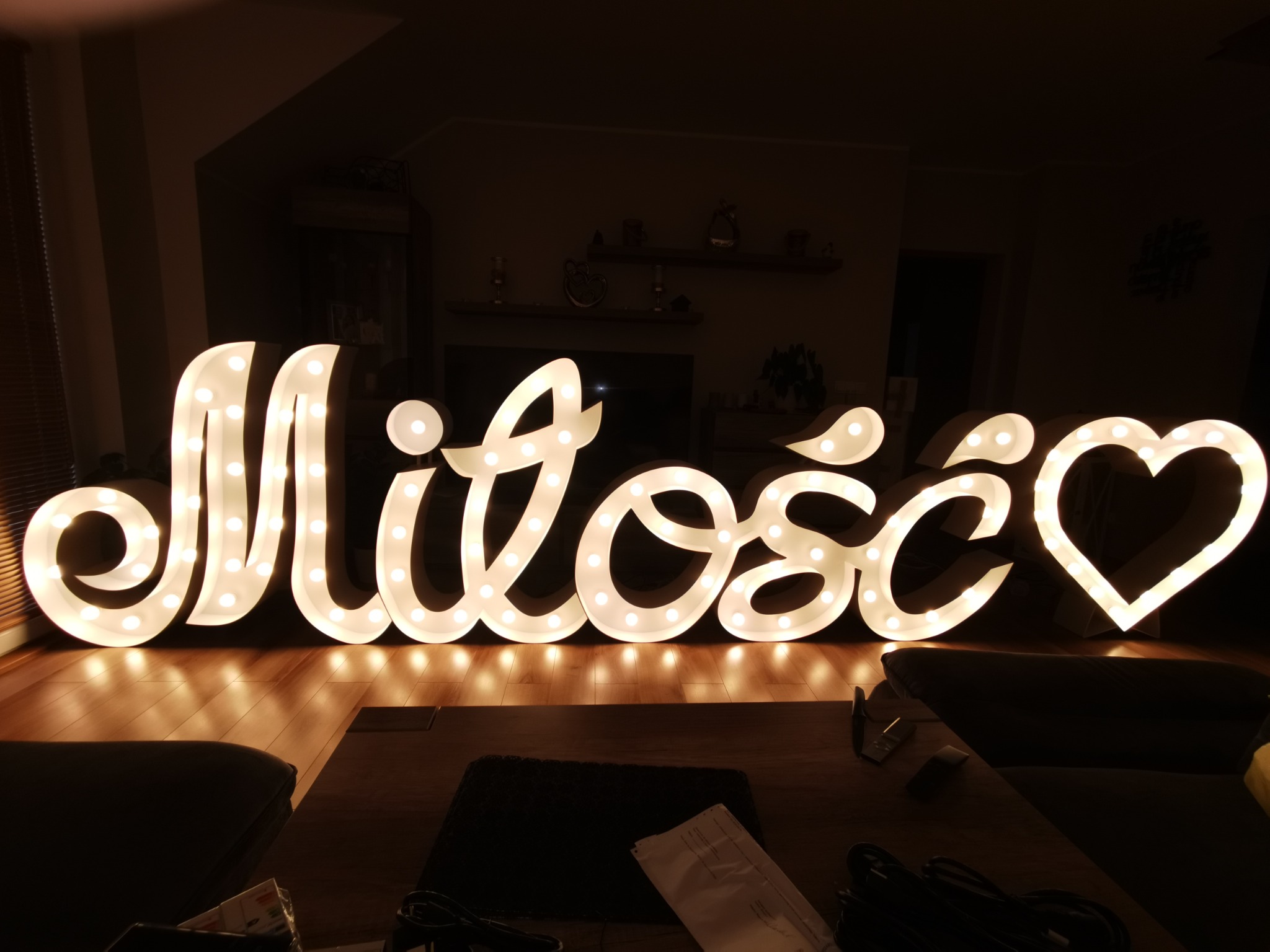 Świecący napis 'Miłość' z żarówkami LED, ustawiony na podłodze w pomieszczeniu, z sercem zamiast ostatniej litery.