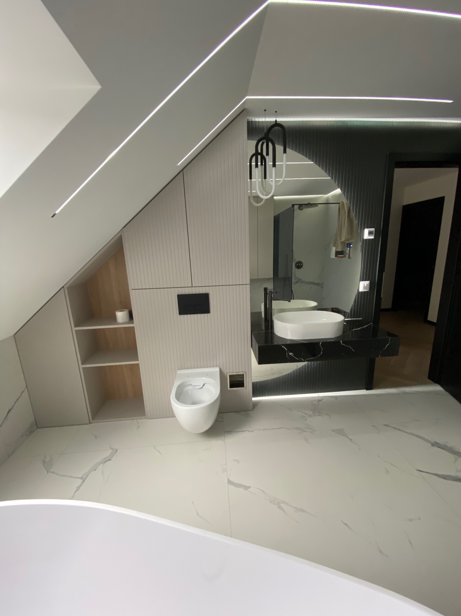 Nowoczesna łazienka na poddaszu z białymi płytkami imitującymi marmur, wiszącą toaletą, umywalką nablatową na czarnym blacie i oświetleniem LED w suficie.