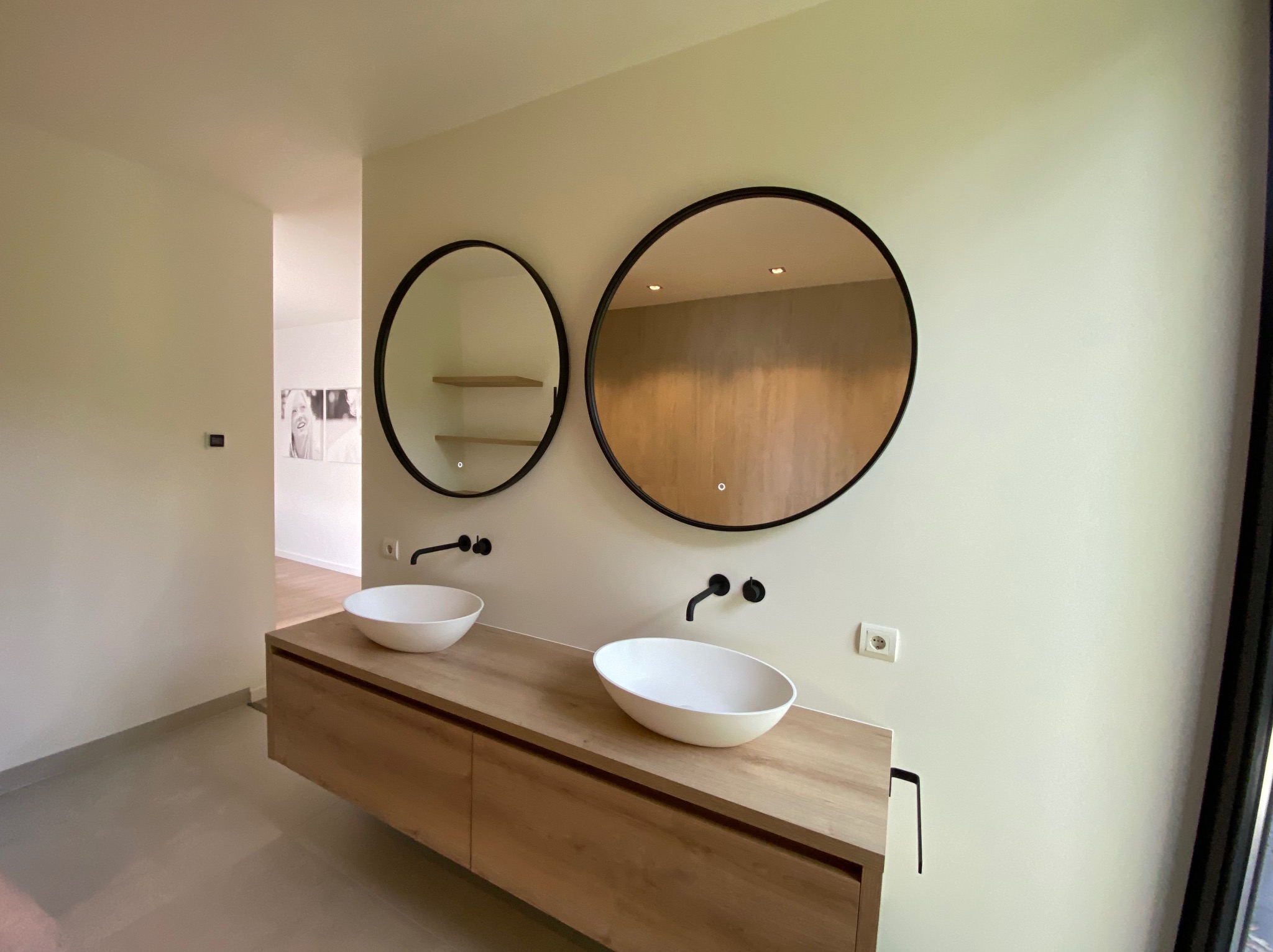 Nowoczesna łazienka z dwoma owalnymi umywalkami nablatowymi, czarnymi bateriami i okrągłymi lustrami z czarnymi ramami, jedno z podświetleniem LED, na drewnianym blacie z szufladami.
