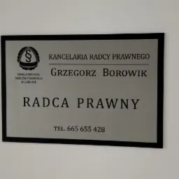 Tabliczka informacyjna Kancelarii Radcy Prawnego Grzegorza Borowika z numerem telefonu, umieszczona na białej ścianie.