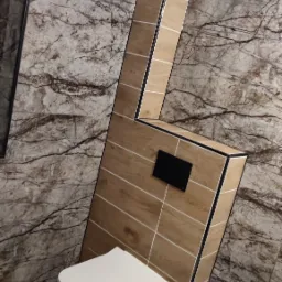 Nowoczesna toaleta podwieszana z zabudową z płytek imitujących drewno i marmurowe ściany w łazience po remoncie.