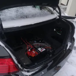 Otwarty bagażnik czarnego samochodu, widoczna instalacja elektryczna i akumulator, na zewnątrz śnieg.