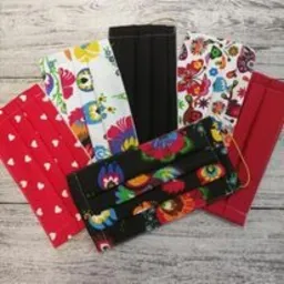 Zestaw maseczek ochronnych z różnych materiałów: czerwonej w białe serduszka, czarnej, czerwonej oraz dwóch wzorzystych w kwiaty i inne motywy, ułożonych na jasnym drewnianym tle.