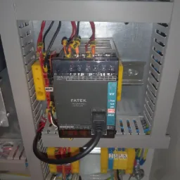 Panel sterowania FATEK z podłączonymi przewodami wewnątrz metalowej szafy, widoczne żółte złączki i oznaczenia na kablach.