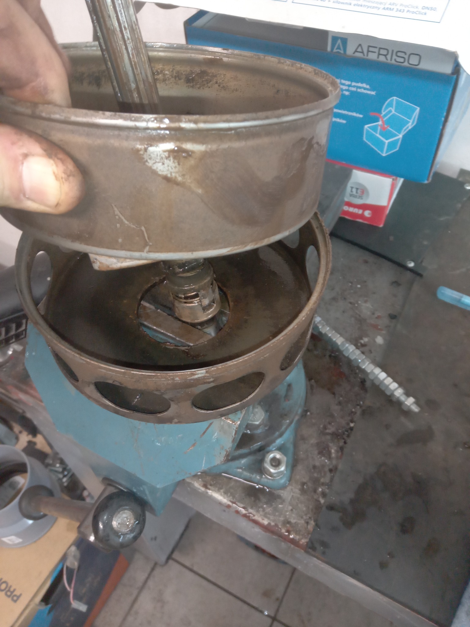 Demontaż lub naprawa uszkodzonego, zardzewiałego elementu pieca CO w warsztacie, widoczny uchwyt imadła i opakowanie AFRISO w tle.