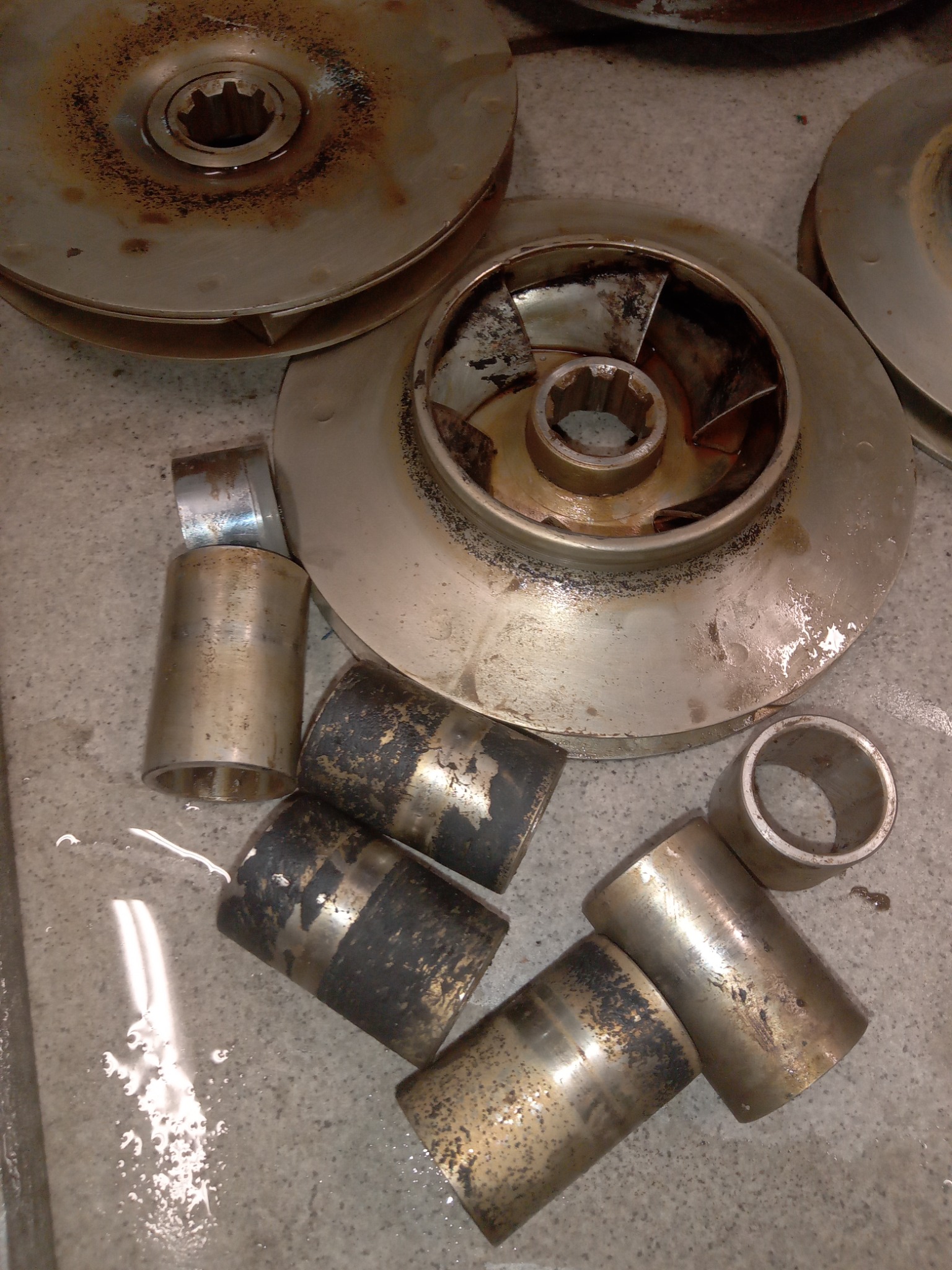 Zdemontowane, zardzewiałe wirniki i tuleje pomp, leżące na mokrej, betonowej posadzce, ukazujące zużycie i potrzebę konserwacji.