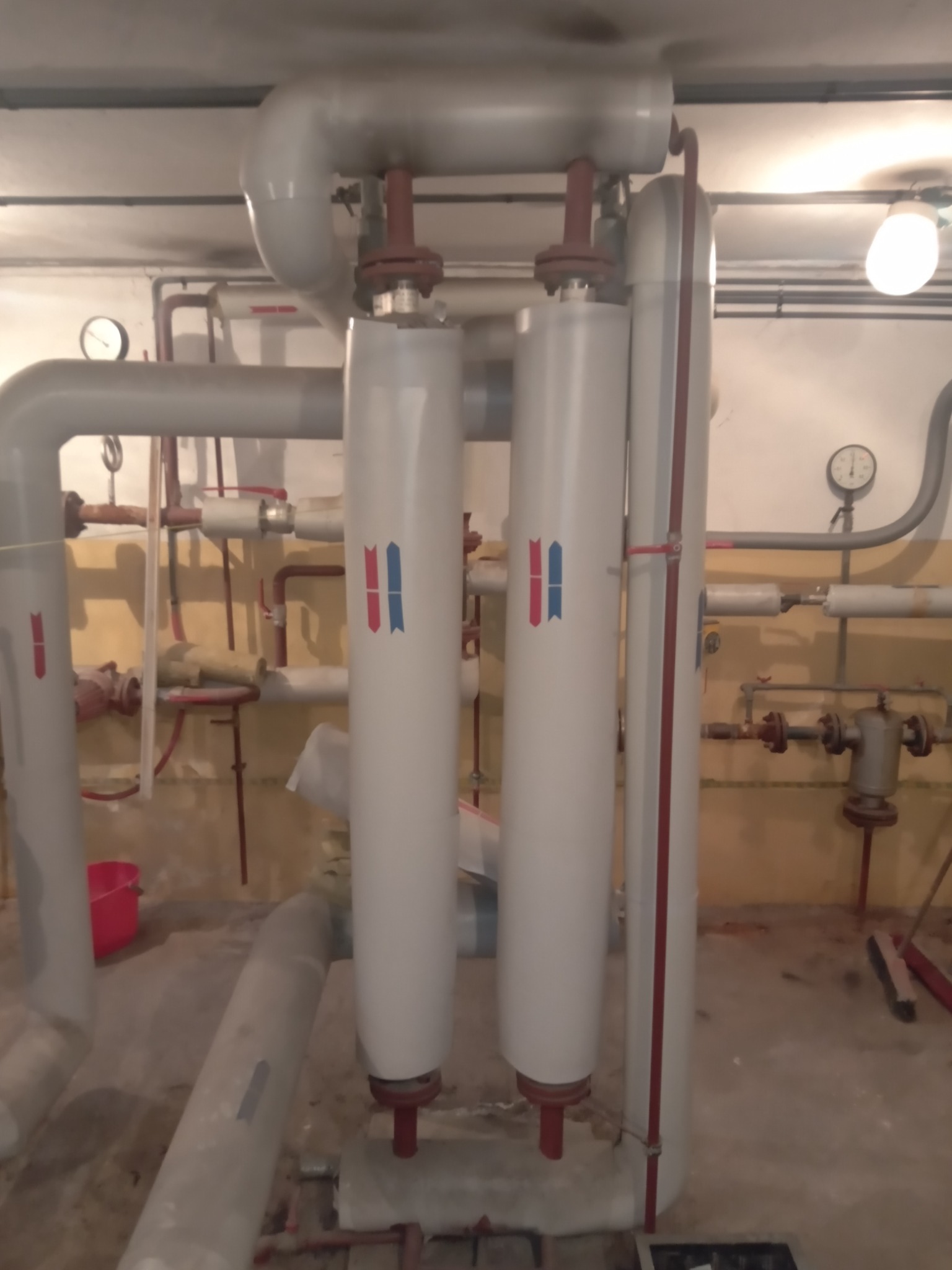 Złożona instalacja grzewcza z rurami i dwoma pionowymi zbiornikami z oznaczeniami w piwnicy we Wrocławiu, widoczne manometry i elementy sterujące.