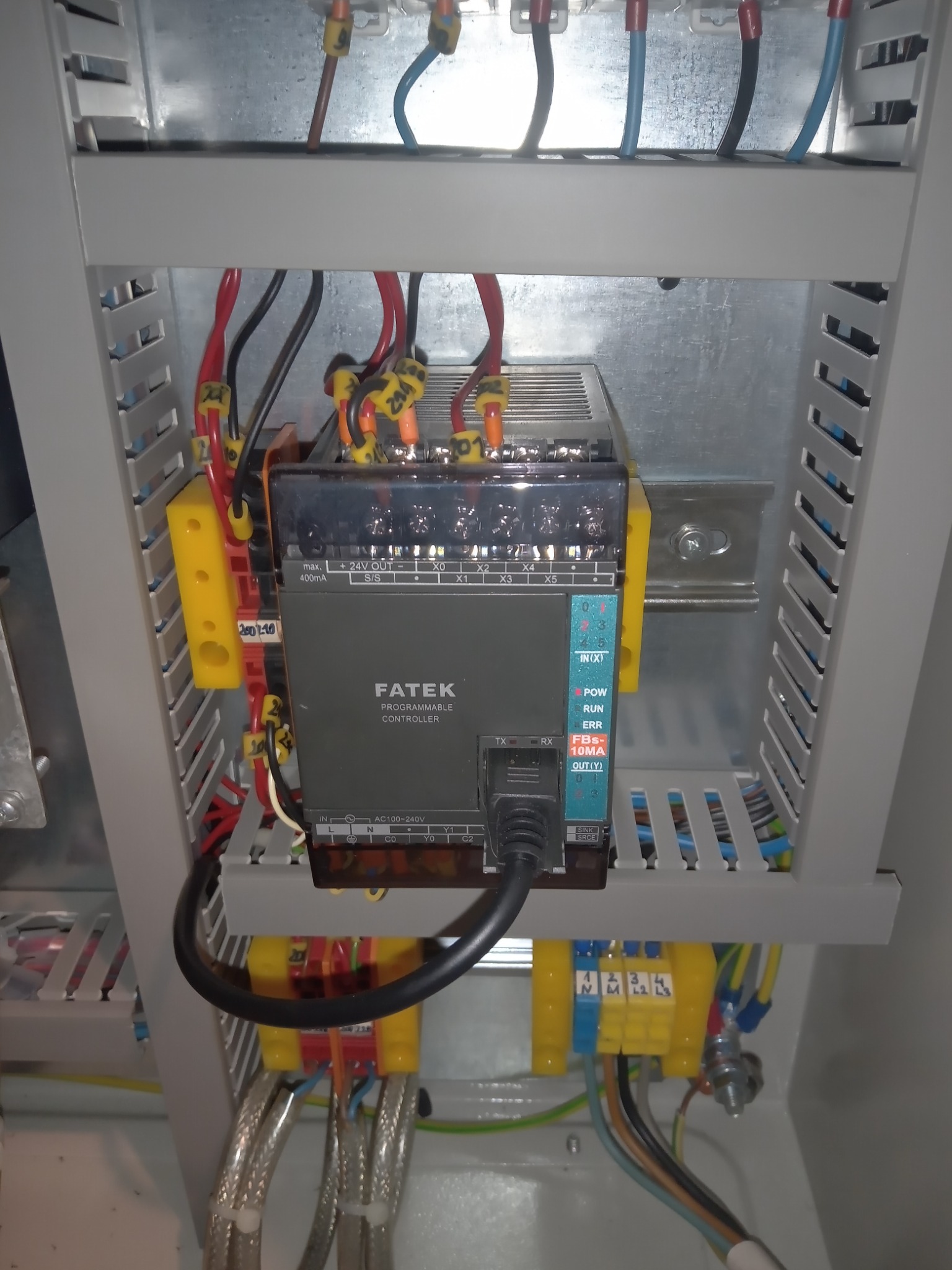 Panel sterowania FATEK z podłączonymi przewodami wewnątrz metalowej szafy, widoczne żółte złączki i oznaczenia na kablach.