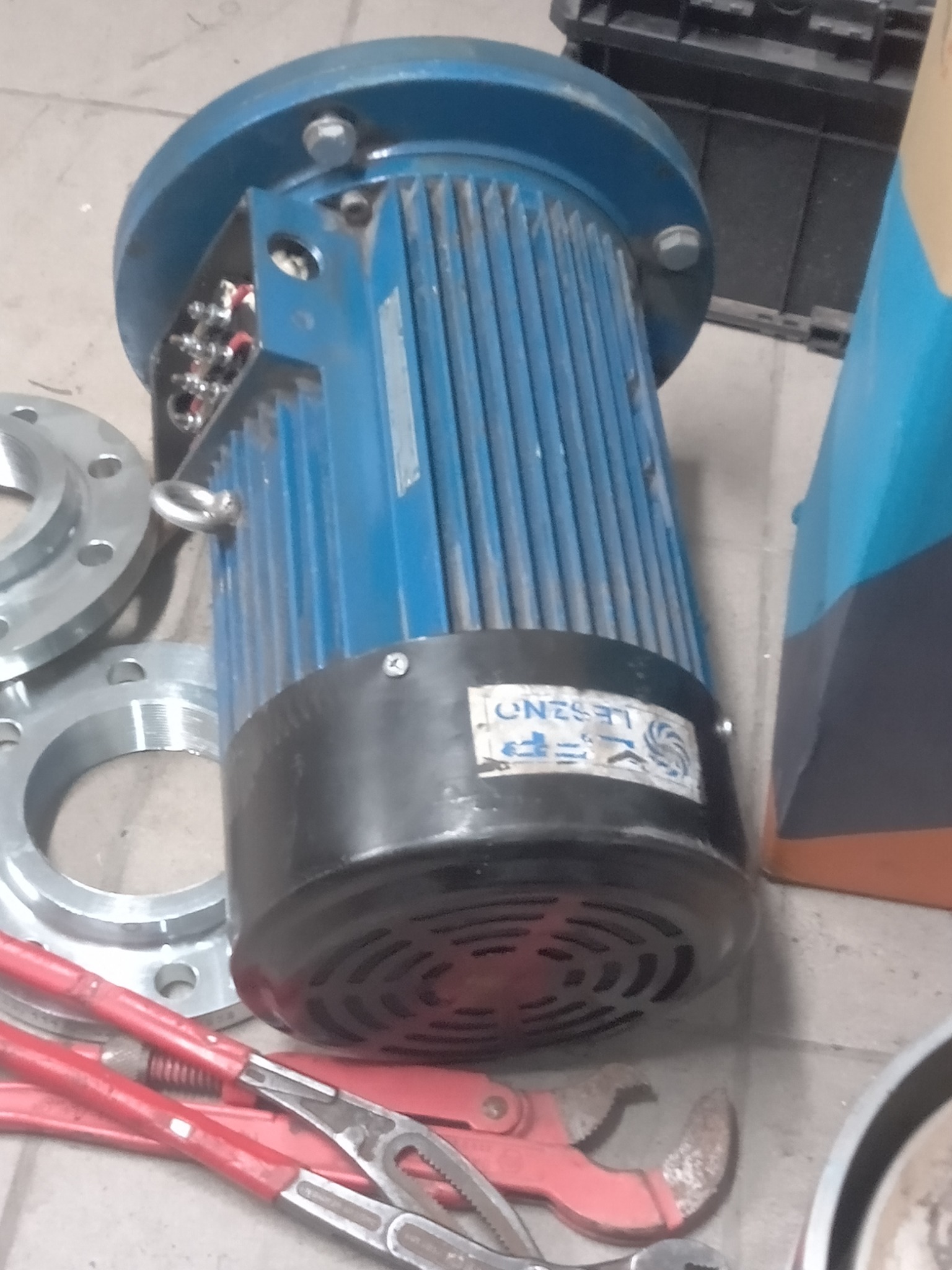 Niebieski silnik elektryczny z widocznymi zaciskami elektrycznymi, obok flansze i czerwone klucze nastawne na podłodze.