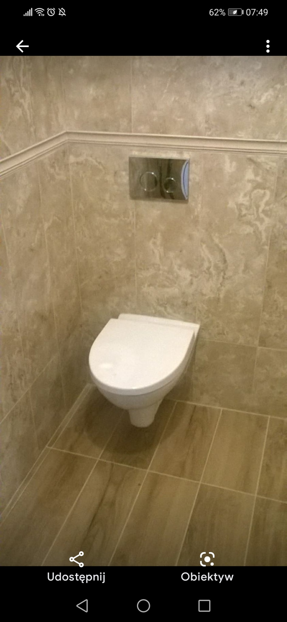 Ściana z beżowych płytek imitujących marmur w łazience w Częstochowie, z podwieszaną toaletą i chromowanym panelem spłukującym.