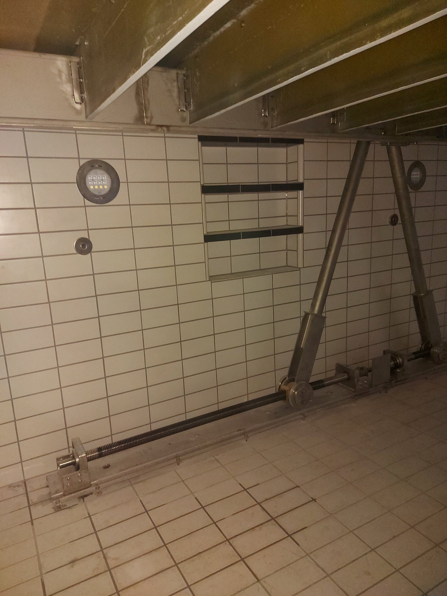 Wzmocnienie konstrukcji stropu w pomieszczeniu wyłożonym płytkami, widoczne metalowe podpory i śruba rzymska, oświetlenie punktowe w suficie.