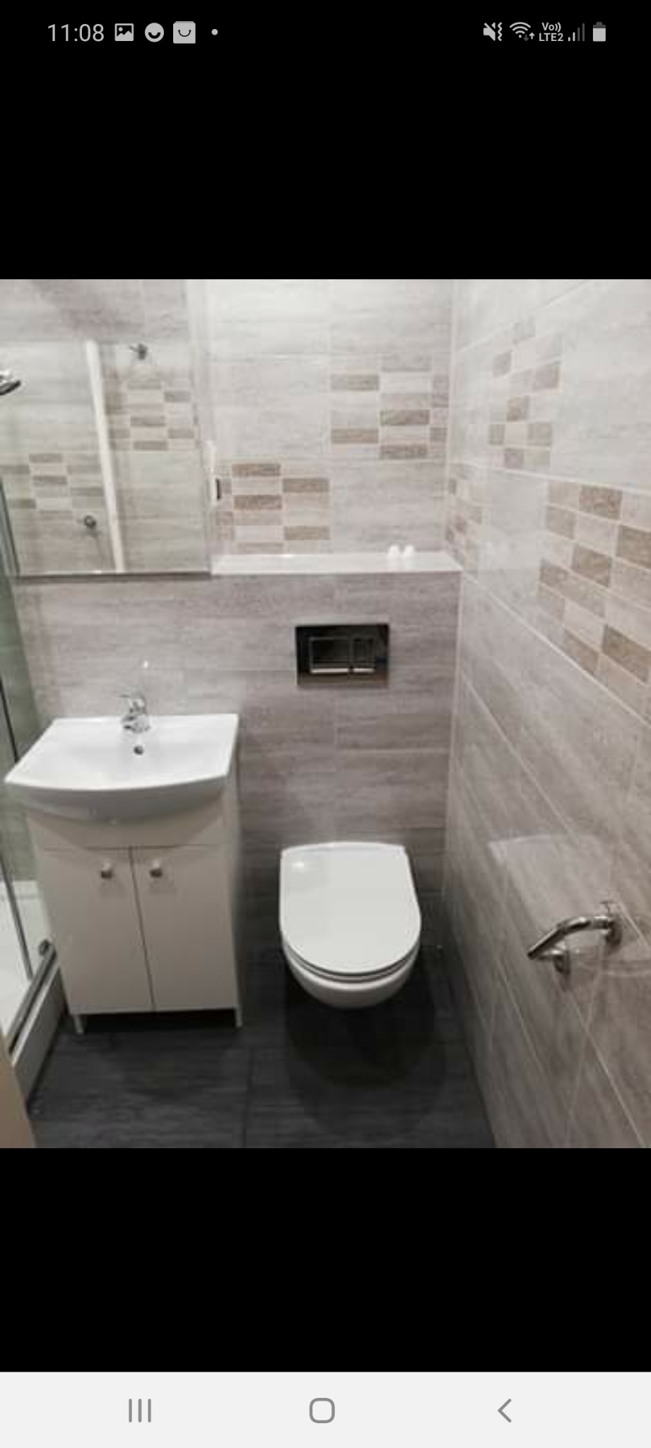 Nowoczesna łazienka w szaro-beżowej kolorystyce z podwieszaną toaletą, umywalką z szafką i kabiną prysznicową z widocznym fragmentem. Na ścianach płytki imitujące drewno z dekoracyjnym pasem.