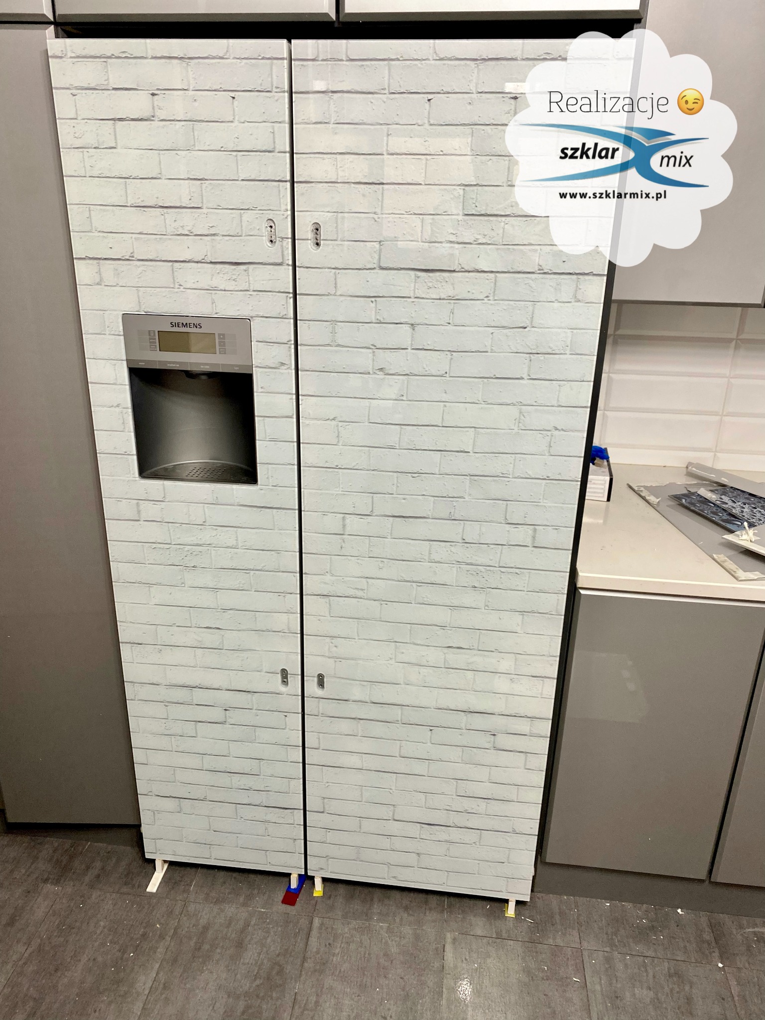 Lodówka Siemens oklejona folią z motywem białej cegły, widoczna w kuchni podczas montażu z użyciem podkładek poziomujących.
