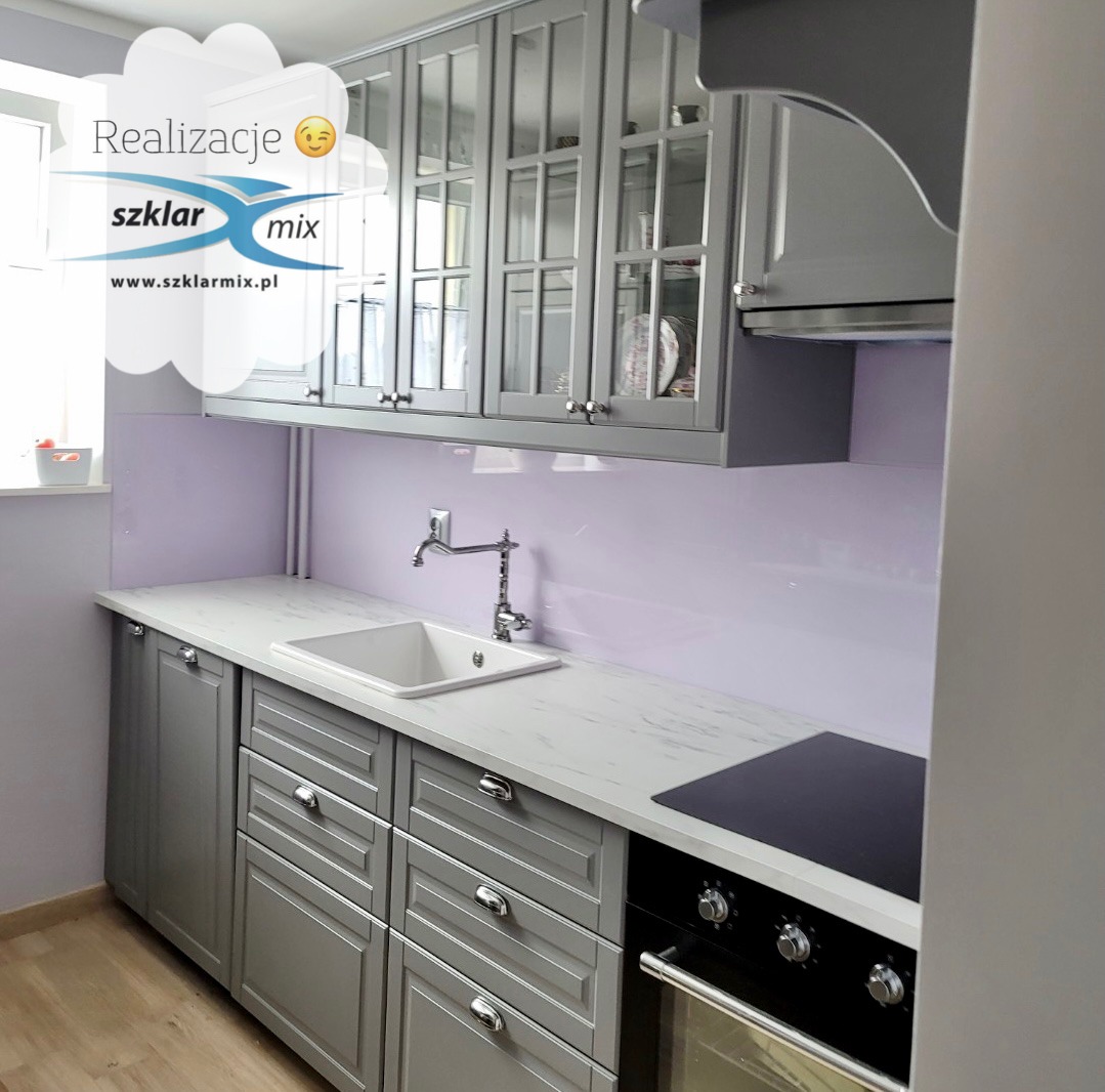 Szklany panel lacobel w pastelowym fioletowym odcieniu, zamontowany jako ochrona ściany nad blatem kuchennym z białym zlewem i chromowaną baterią, w szarej kuchni z przeszklonymi szafkami wiszącymi.