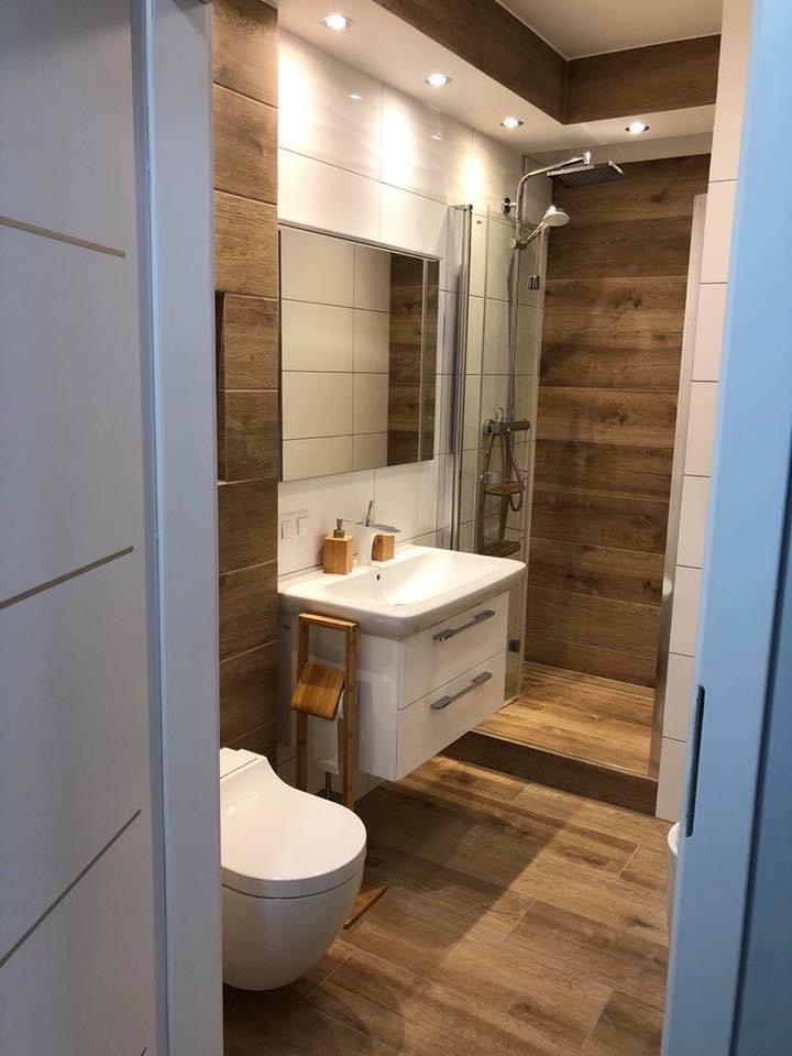 Nowoczesna łazienka z drewnopodobnymi płytkami, kabiną prysznicową typu walk-in i podwieszaną szafką z umywalką.