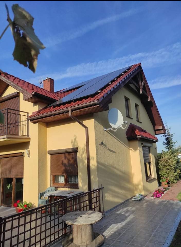 Żółty dom jednorodzinny z panelami słonecznymi na dachu z czerwonej dachówki, widok z boku w słoneczny dzień.