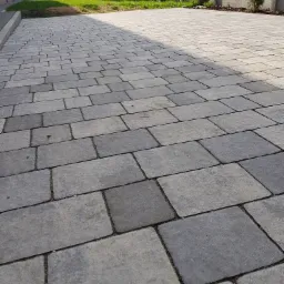 Szara kostka brukowa ułożona na posesji, widok z perspektywy chodnika w kierunku ogrodzenia i zieleni.